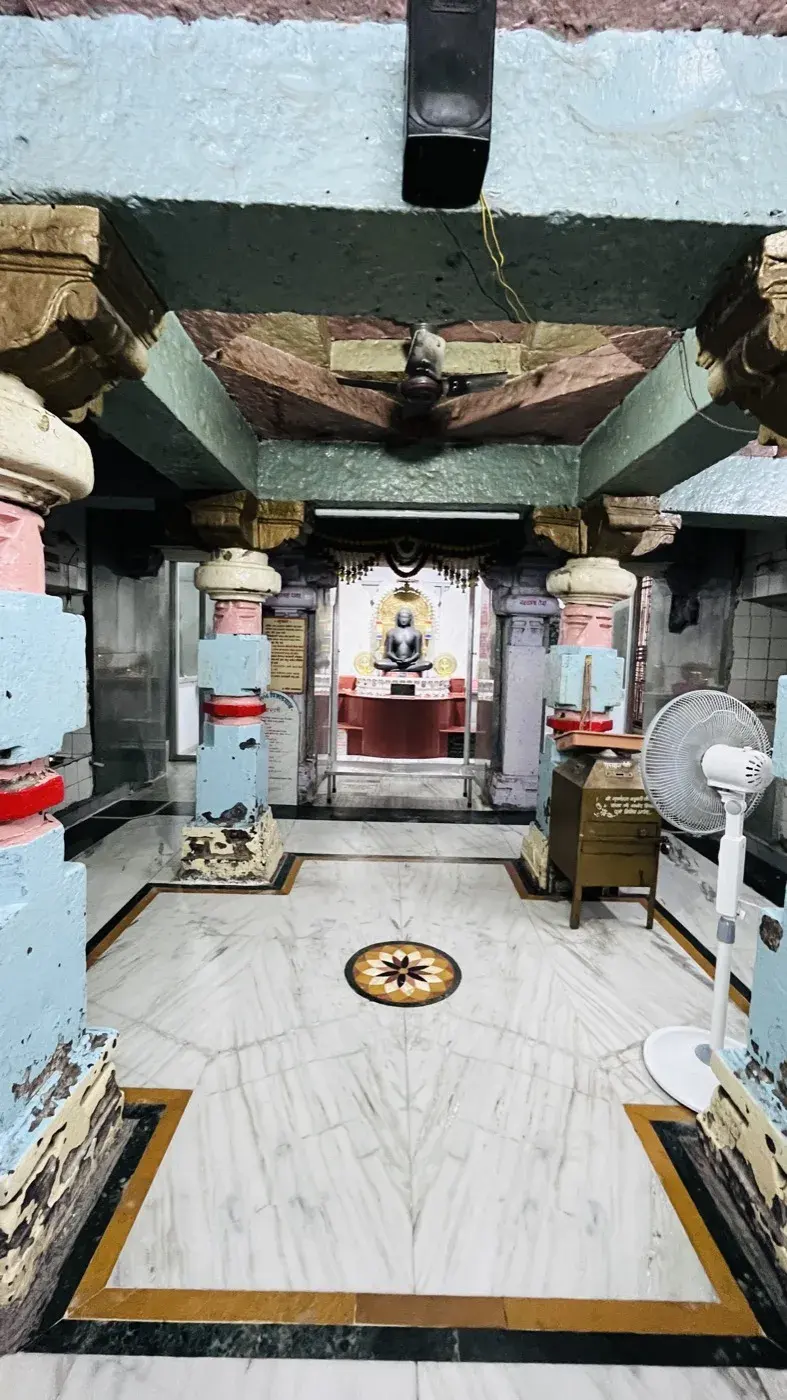 स्तंभों से गर्भगृह की ओर देखा गया सभामंडप, दूर छोर पर माला के नीचे मूलनायक दिखाई देते हैं।