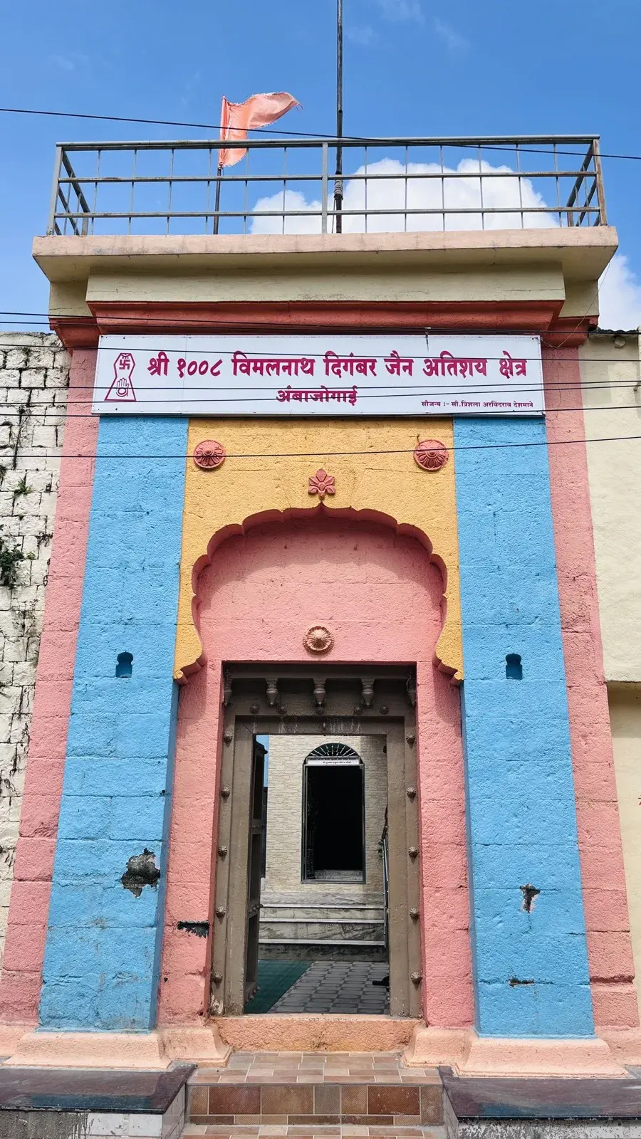 The kshetra's entrance on Jain Galli as it stands today, with visible wear on the paint and patched masonry.
